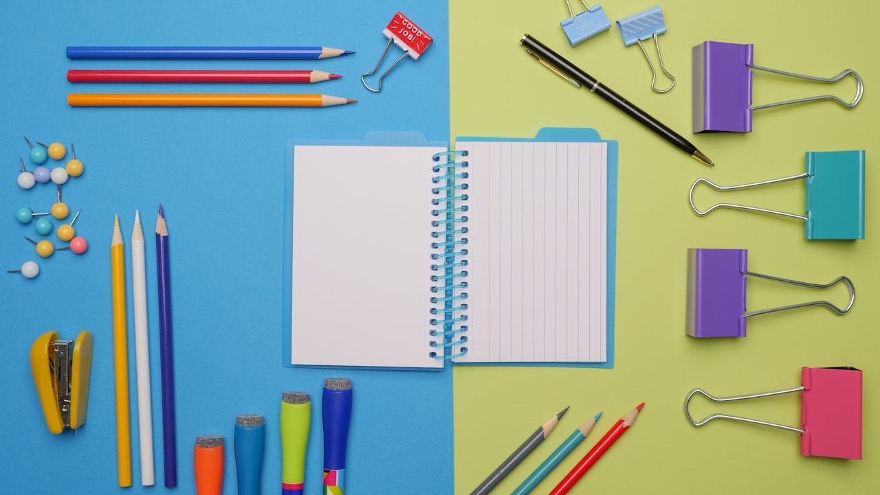 Flat lay of colorful school supplies on a blue and green background, featuring notebooks, binder clips, and stationery.